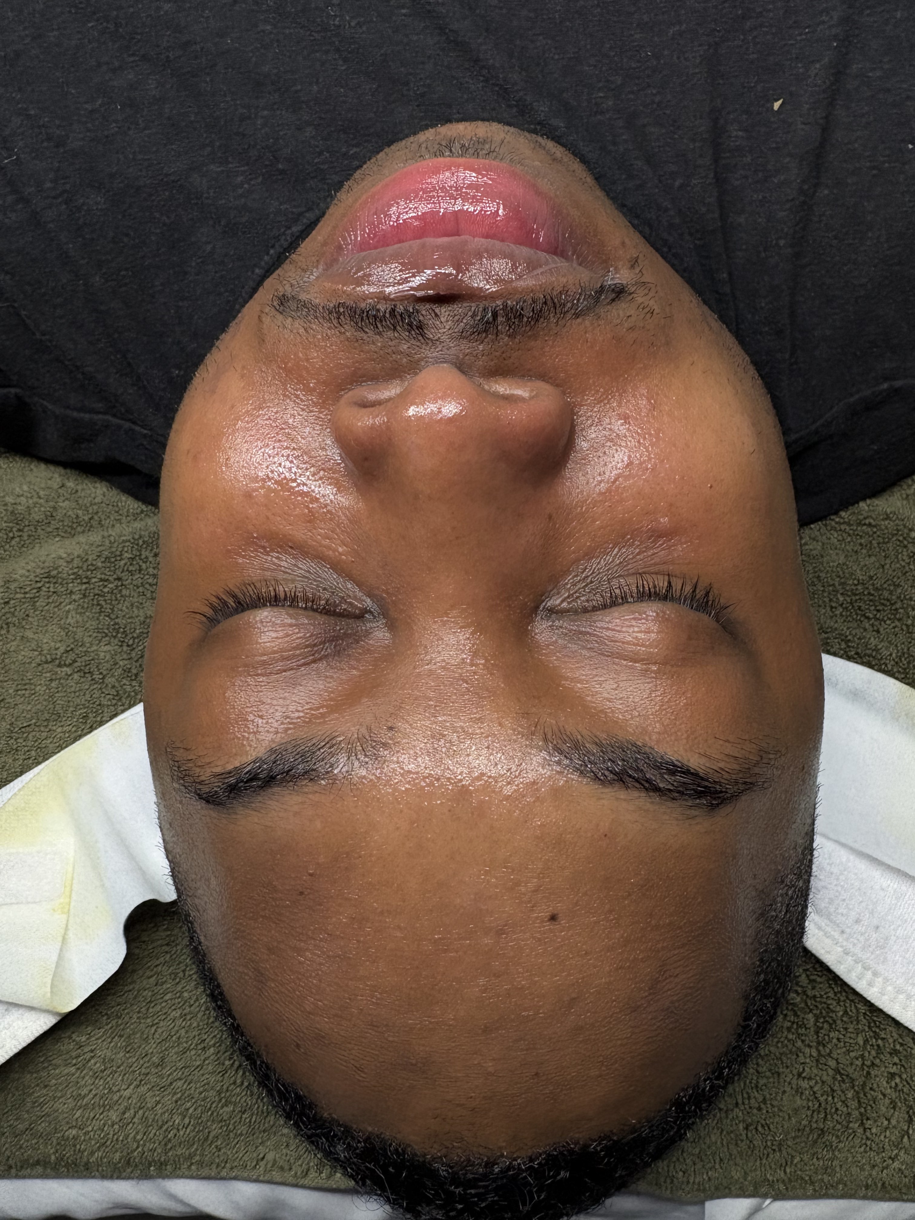 Male client with deeper skin tone resting after a clarifying Gentlemen's Facial, skin looking calm and even